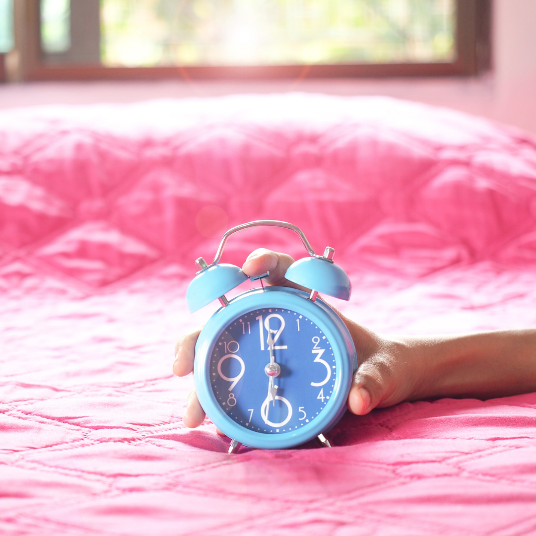 hand holding blue alarm clock on pink bed